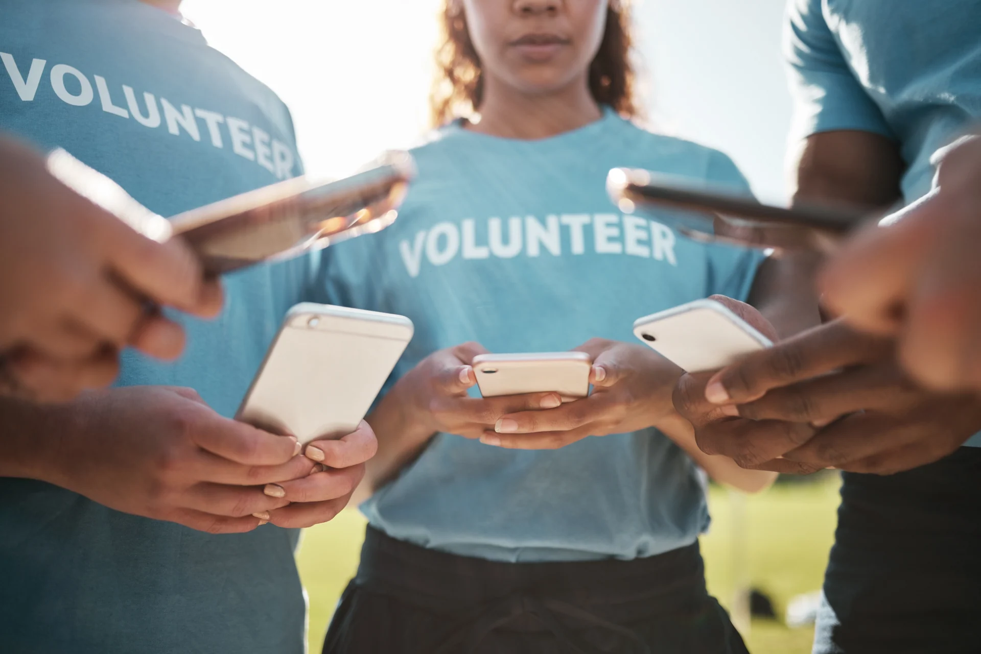 Volunteer, park and hands of people with phone for social media, online chat and charity website. Community service, teamwork and men and women typing on smartphone outdoor for recycle cleaning blog